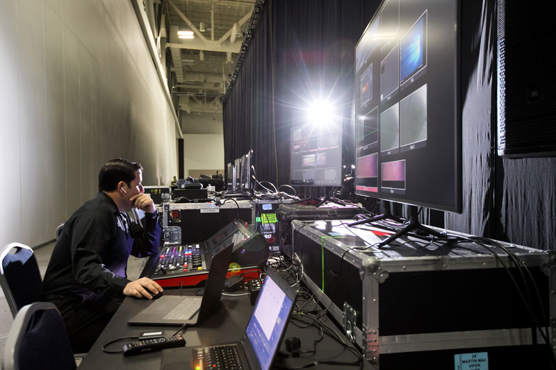 Event production team member evaluates audio visual technology behind stage of a live event