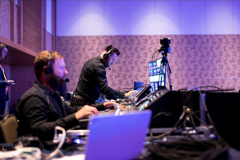 Vario production team in the back of a room monitoring the audio and visual equipment during a live event
