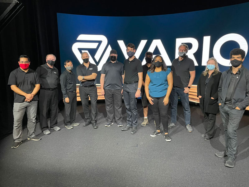 Eleven Vario team members in front of a large Vario banner at an event