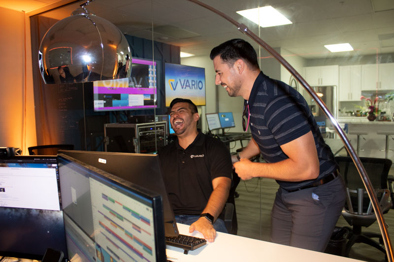 Two teammates laughing together while looking at a computer within the Vario office