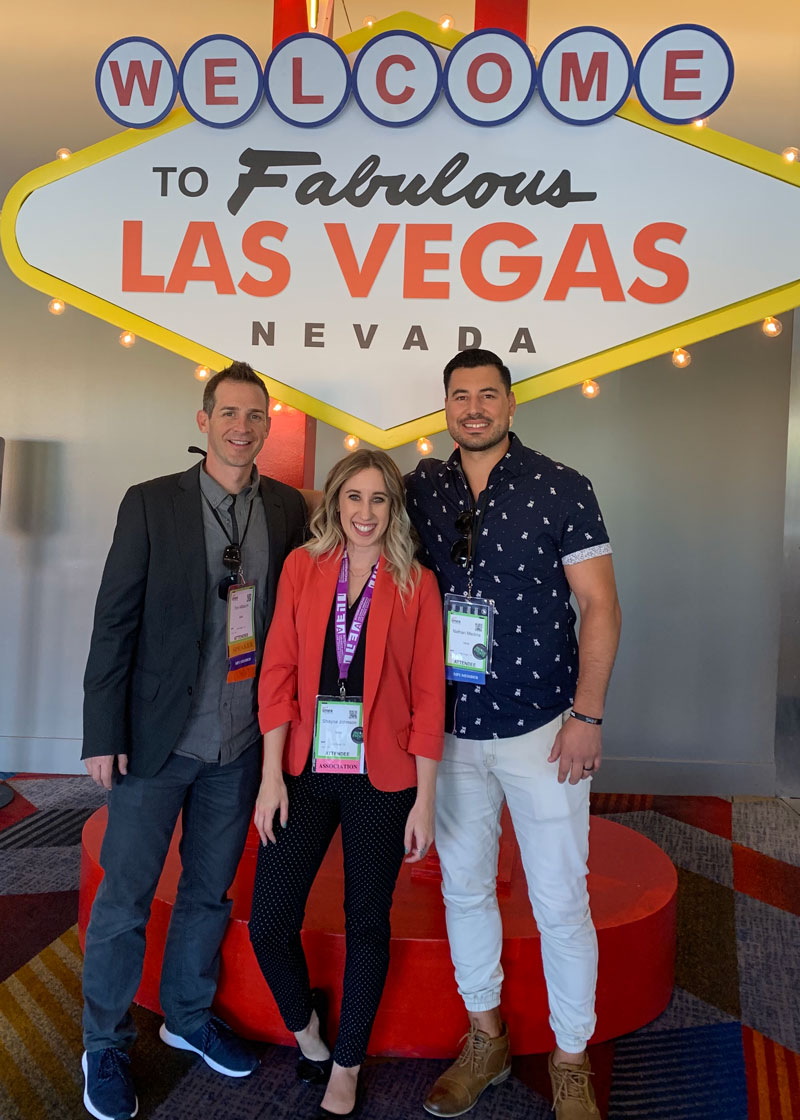 Three teammates smiling and standing in front of a Welcome to Fabulous Las Vegas sign