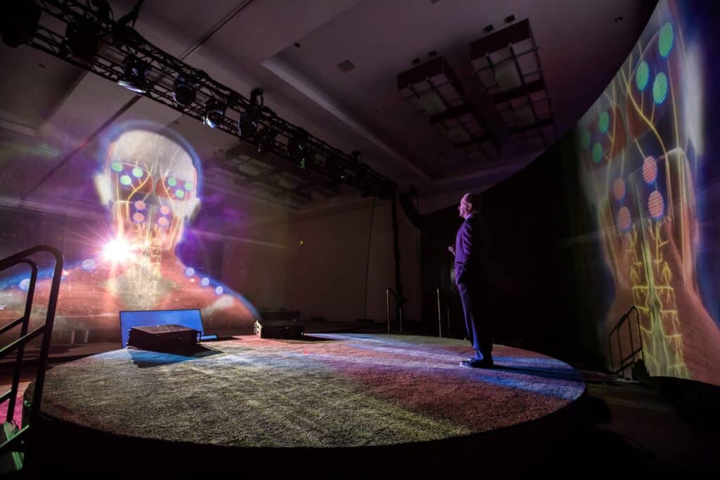 Man looking at the hologram presentation of the human body that is being projected on an event stage