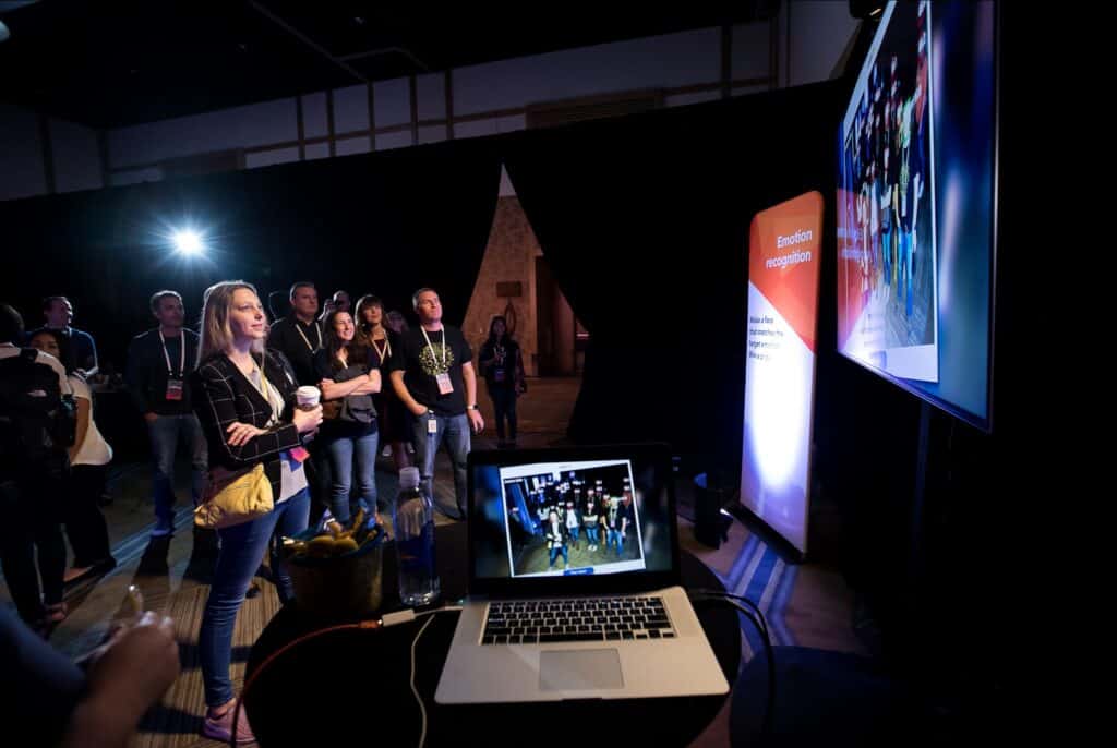 Event attendees testing the facial recognition features of an app on a wide monitor panel