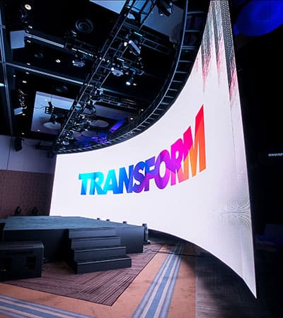 Creative staging setup with a wide curved LED screen panel and black center stage for a Transform event