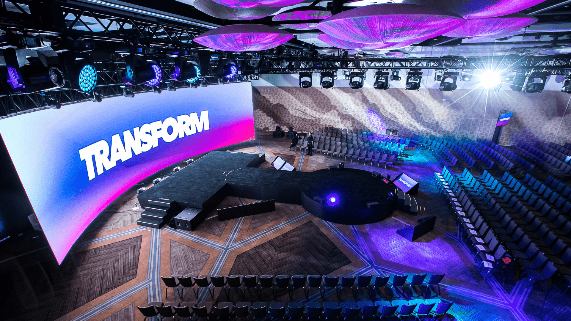 Event stage design for a Transform live event with a large curved screen and blue and purple lighting