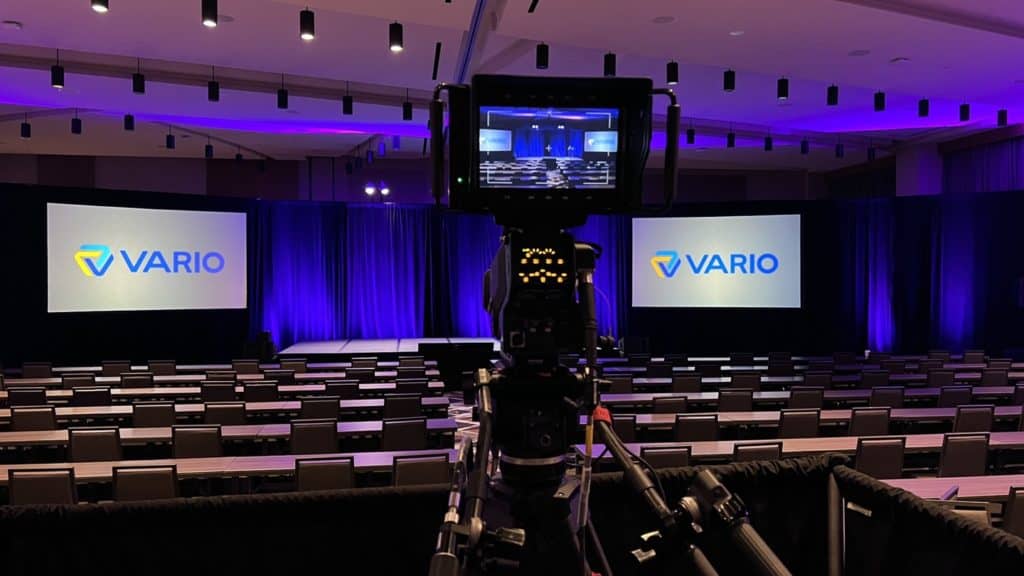 Event production camera is aimed at empty corporate event stage, with empty seats in front.