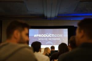 Event attendees converse while waiting for the presentation to start at an event titled #ProductCon.